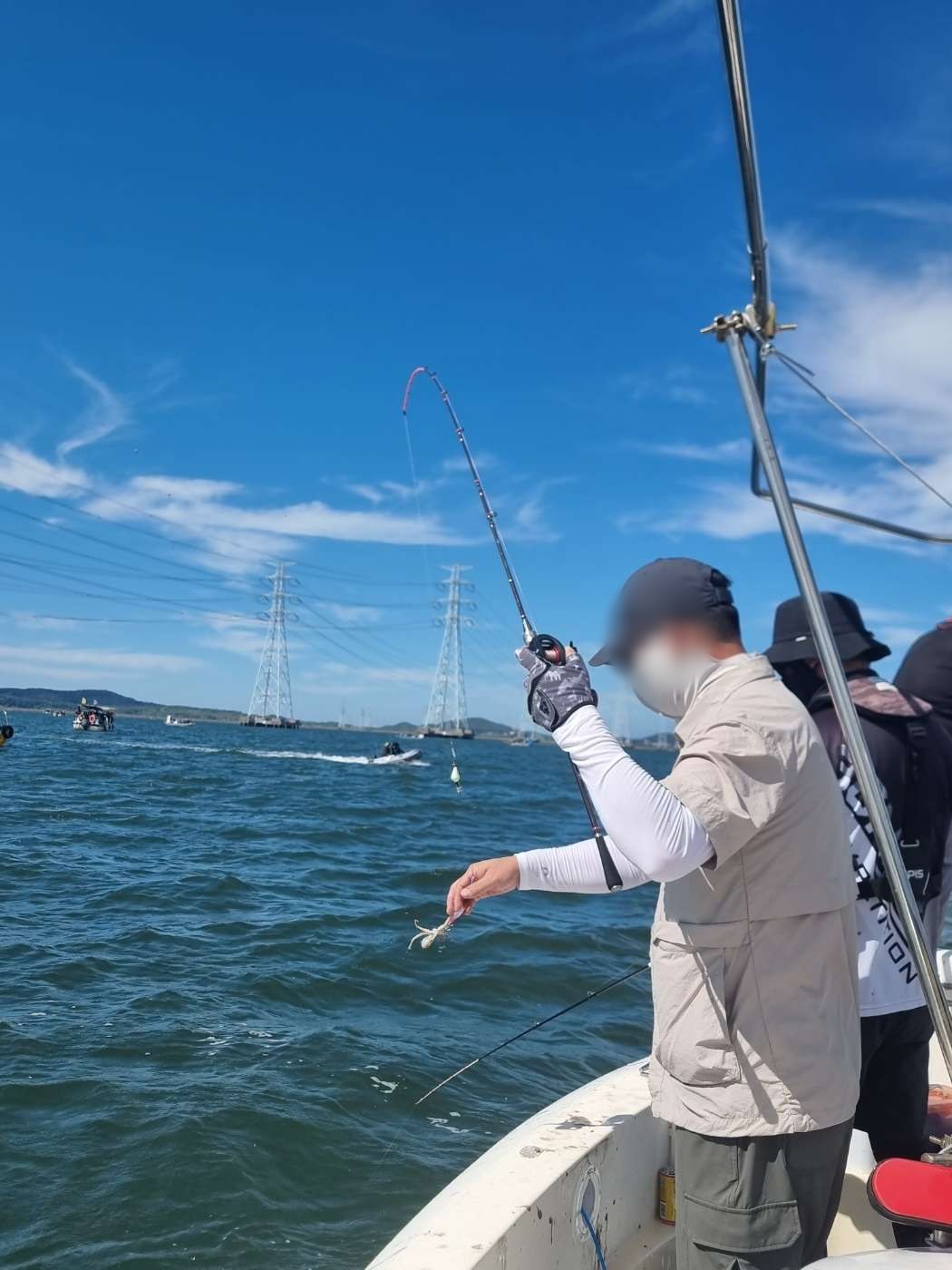 9월 5일 거북섬 시화호 쭈꾸미 조황 사진 2 — 손에 잡힌 쭈꾸미, 뒤로 송전탑과 배들